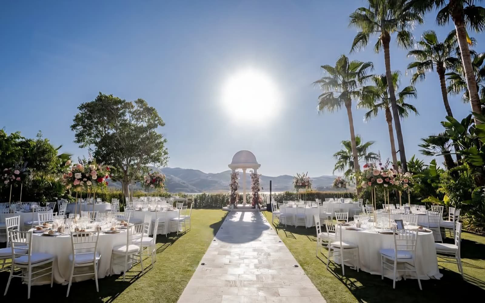Wedding ceremony lawn with round tables and a domed gazebo by the lake