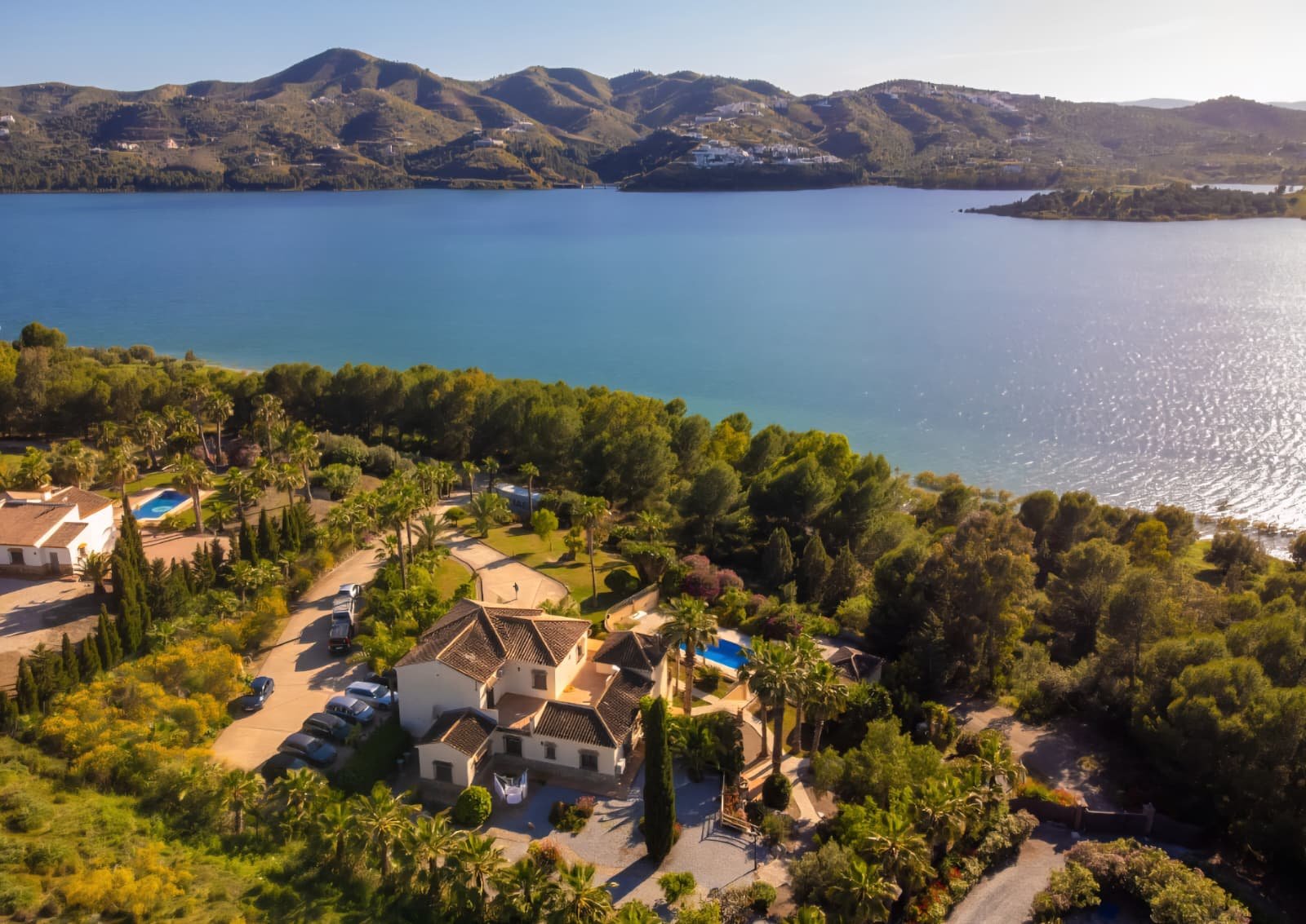 Aerial view of the white villa estate above a turquoise lake with mountain villages behind