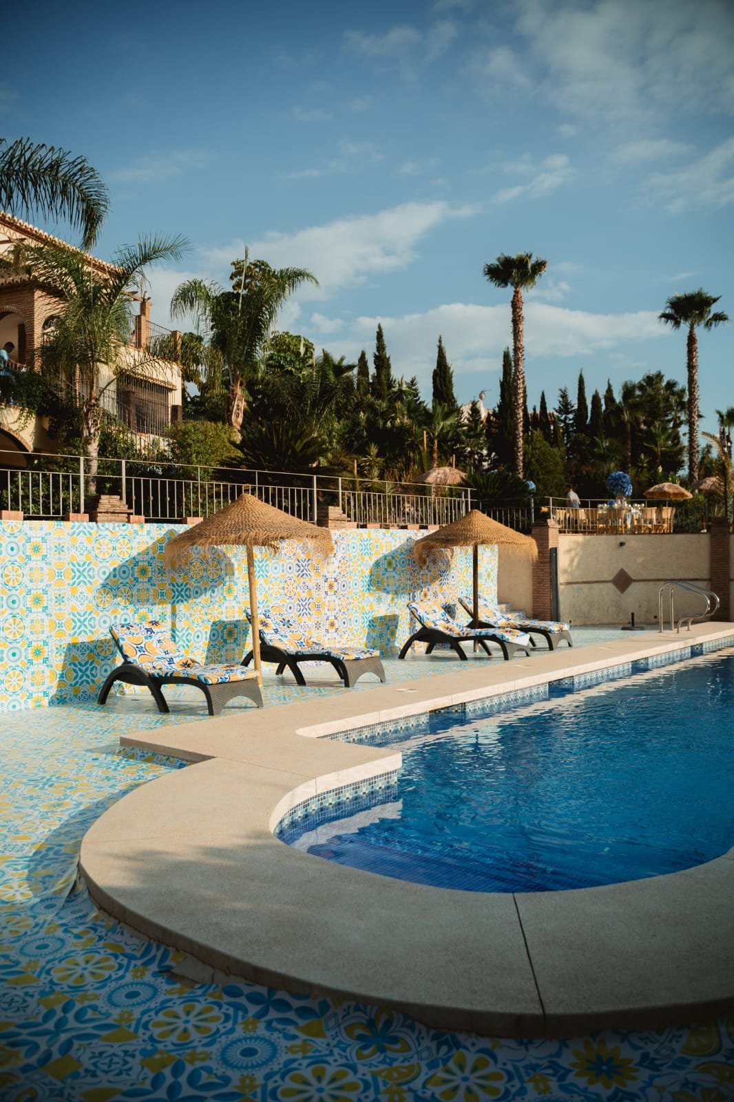 Curved pool with straw umbrellas and lemon-motif patterned tiles