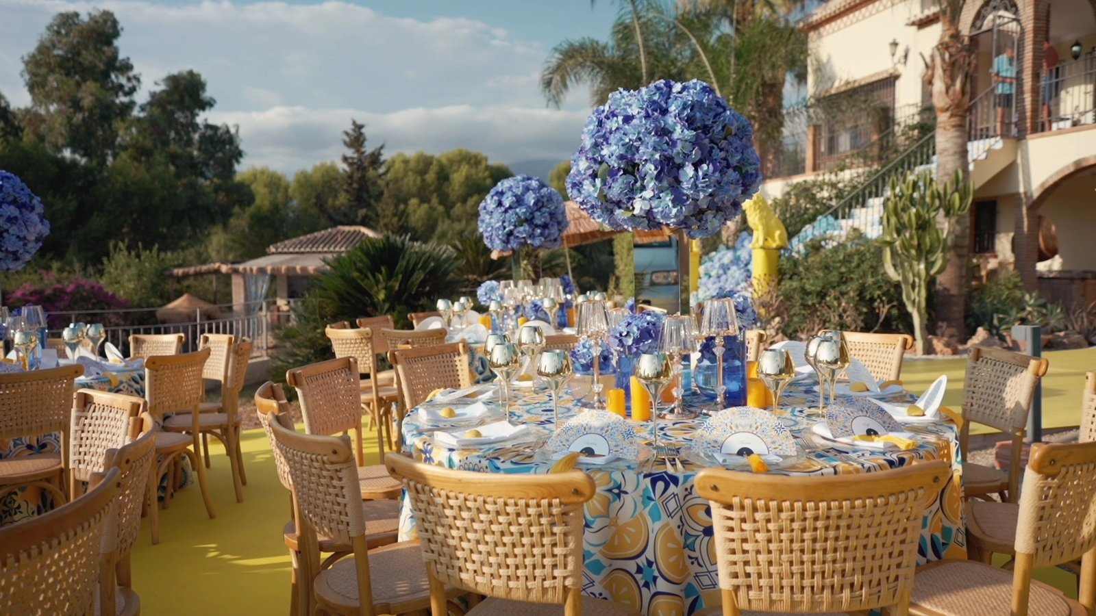 Reception tables with blue hydrangeas on the lawn in front of a cream Andalusian villa