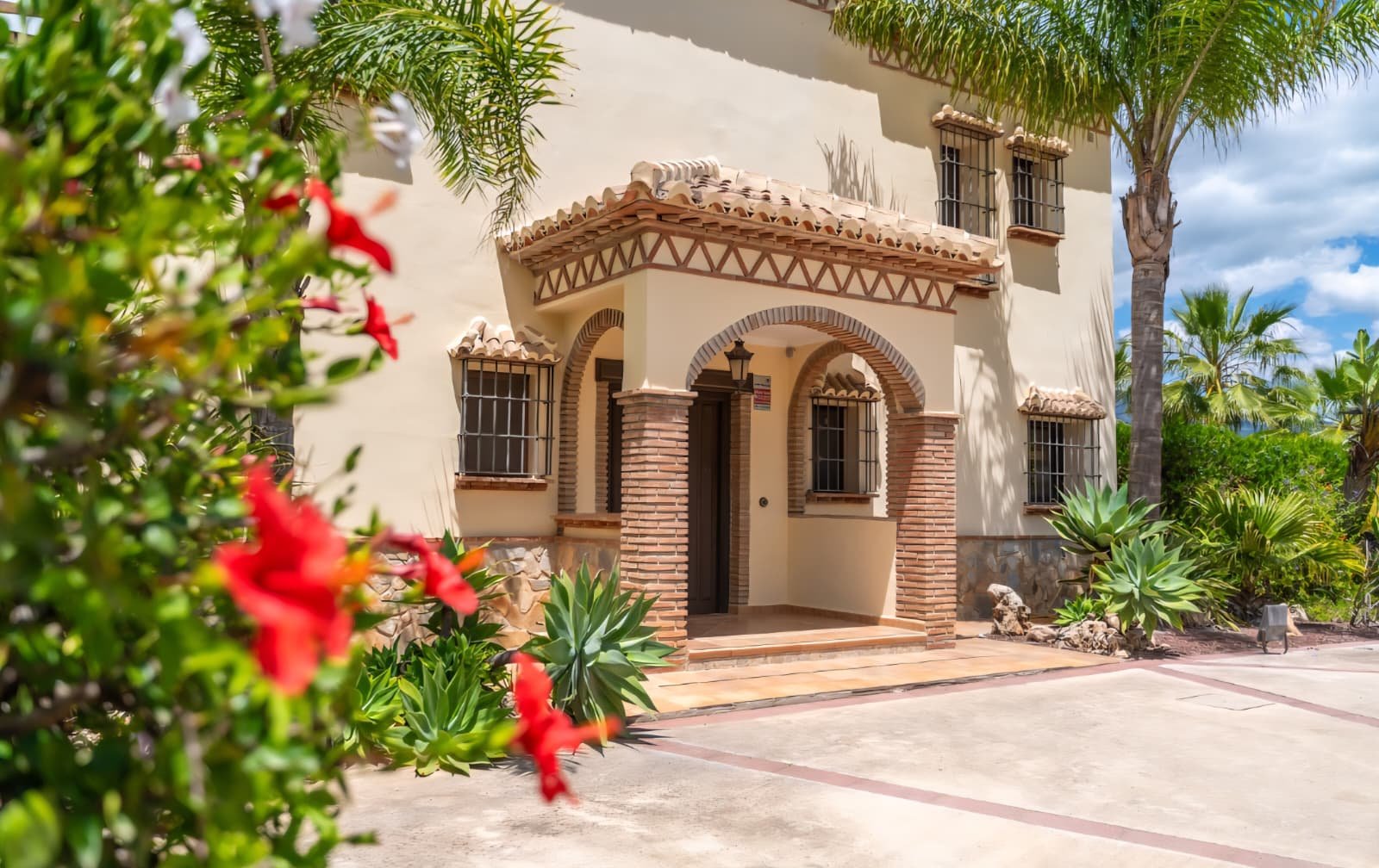 Andalusian villa facade with rustic brick arches and palms under a blue sky