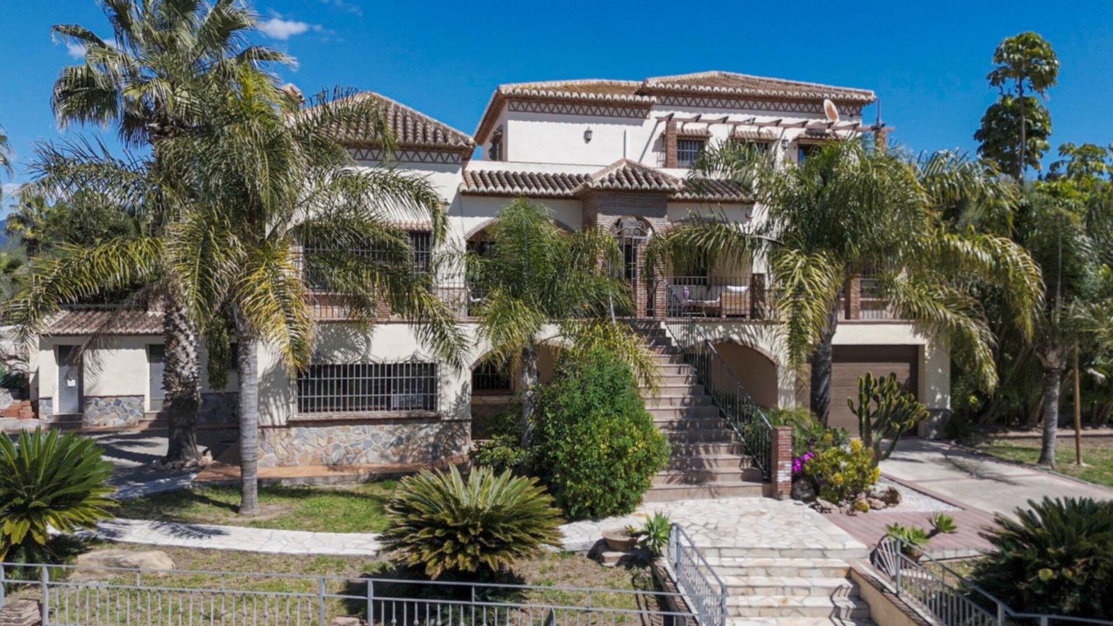 Cream Andalusian villa with terracotta roofs, brick arches and a grand double staircase